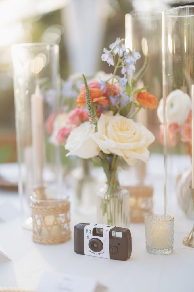 Reception table decorated with candles, colorful bouquets, and a disposable camera.