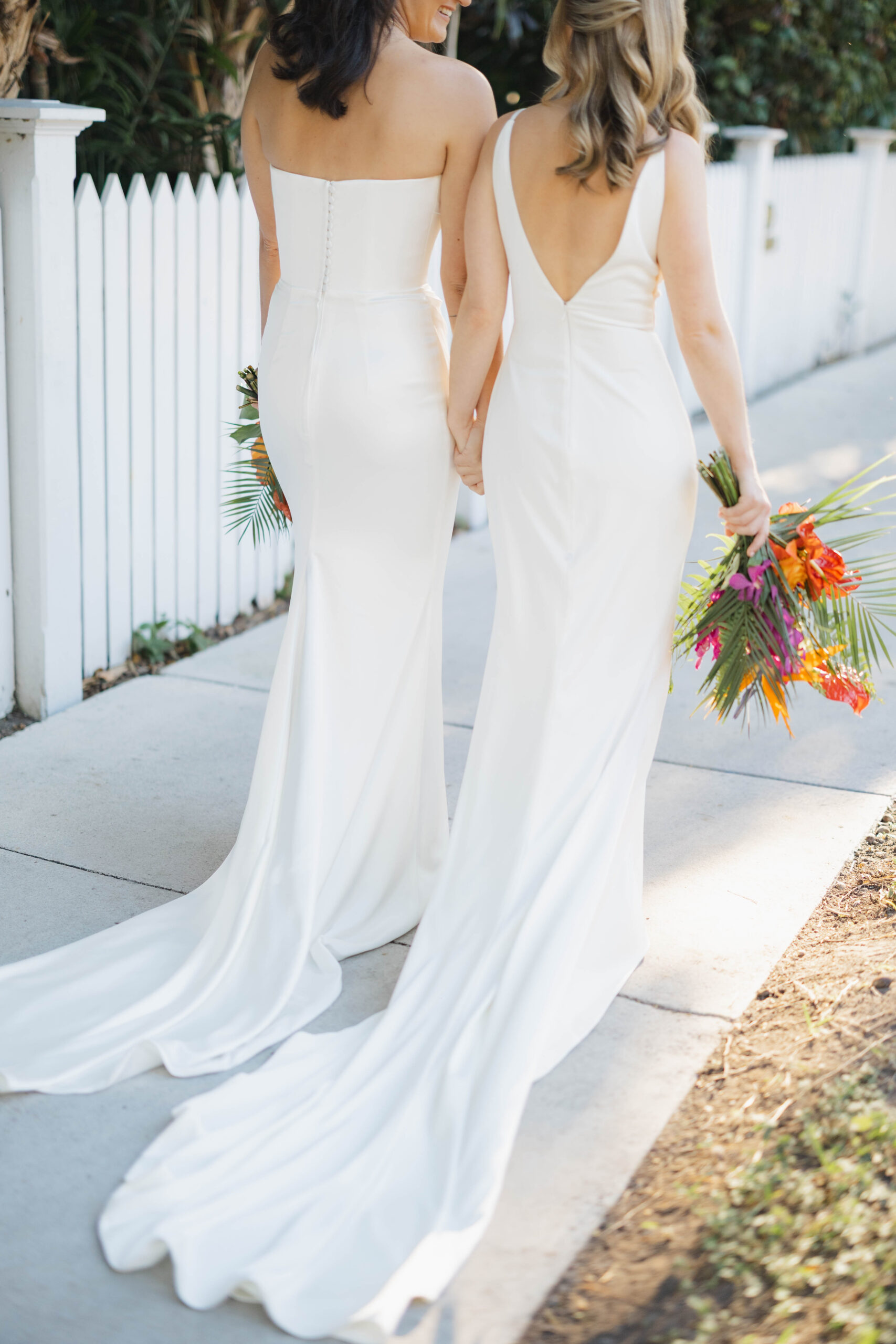 Two brides walk hand in hand holding their tropical flower themed bouquets down the sidewalk in Key West FL