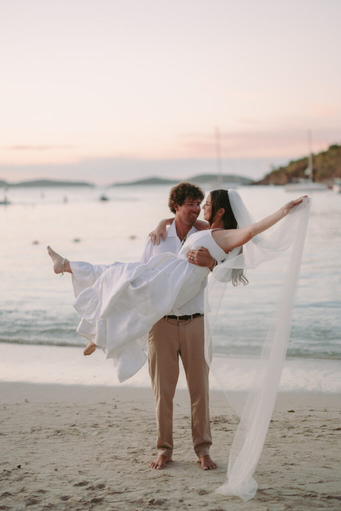 Groom holding bride with veil hanging onto the sand during their St John USVI wedding