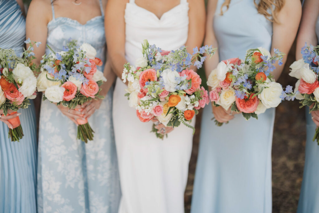 Bride in white dress with bridesmaids in light blue dresses holding colorful bouquets.