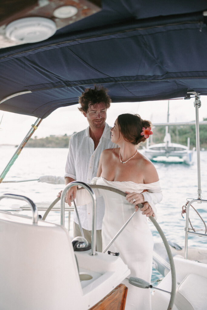 Bride and groom steering their sailboat at sunset