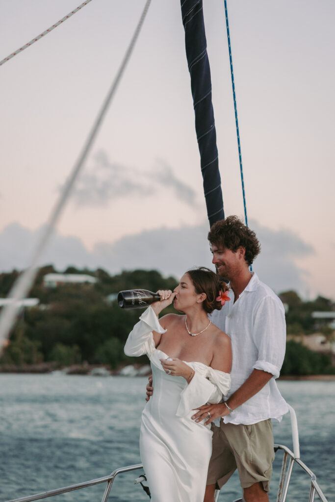 Bride drinking a bottle of champagne on their sailboat after their st john virgin islands wedding