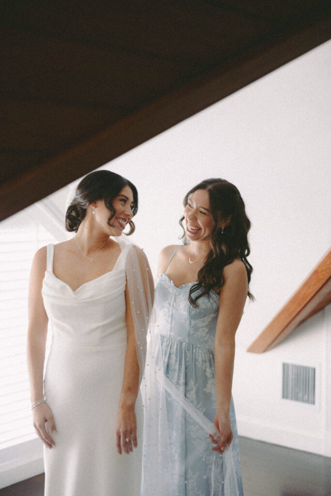 Bride in white dress looking at her bridesmaid in a light blue dress and smiling captured on film