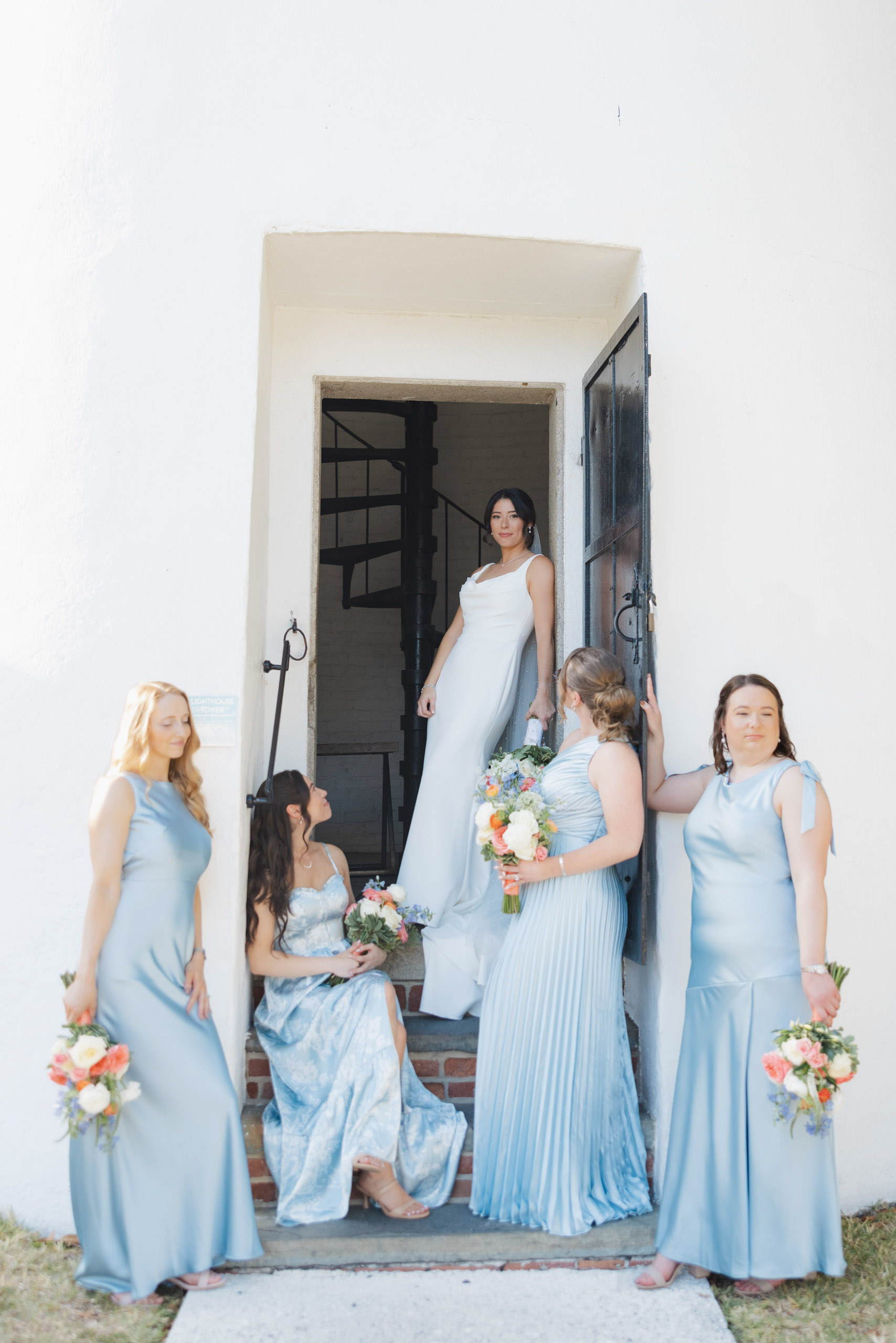 Bride in white dress poses with her bridesmaids in light blue dresses at the Historic Key West Lighthouse.