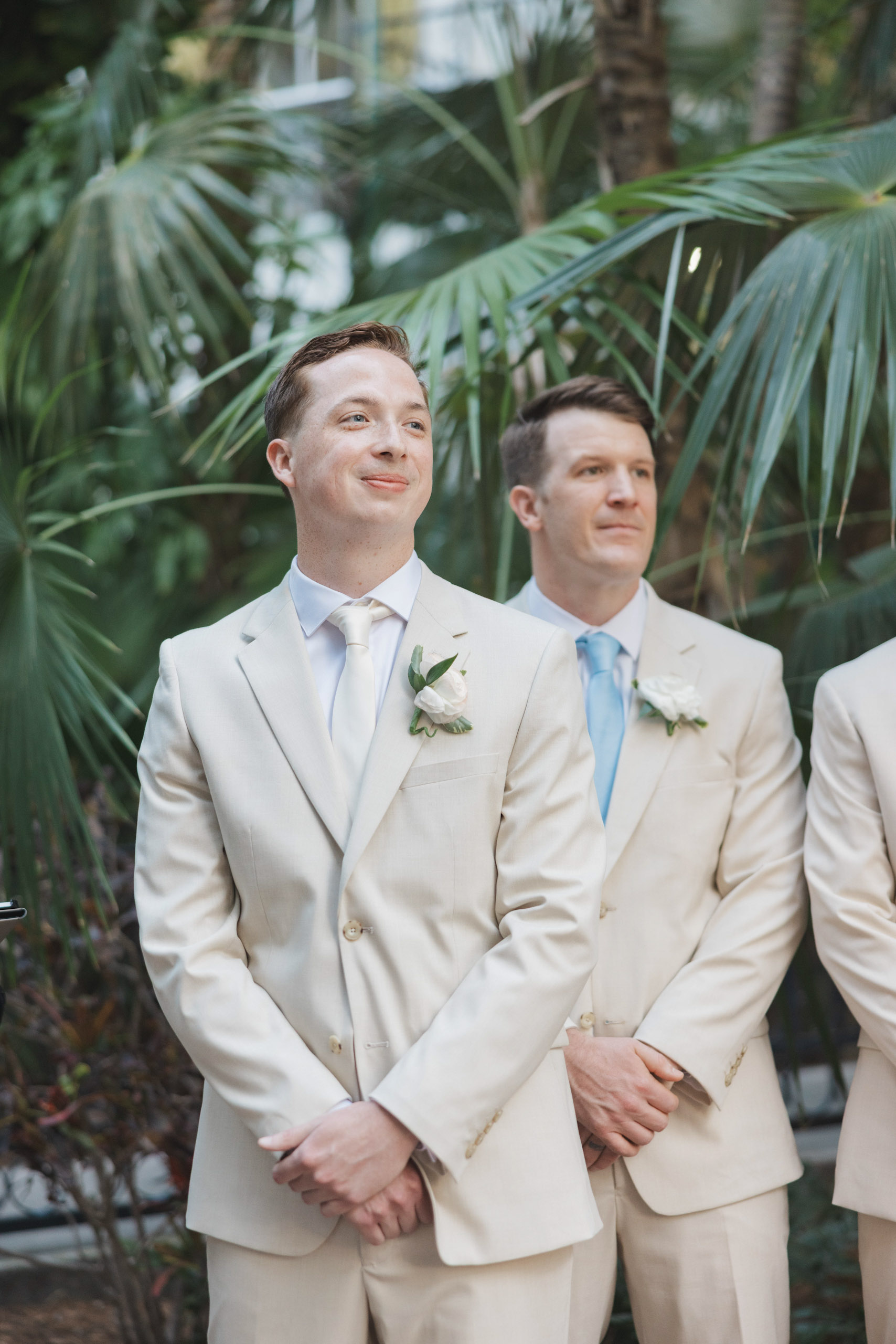 Groom in khaki suit stands at the end of the aisle watching the bride walk down the aisle