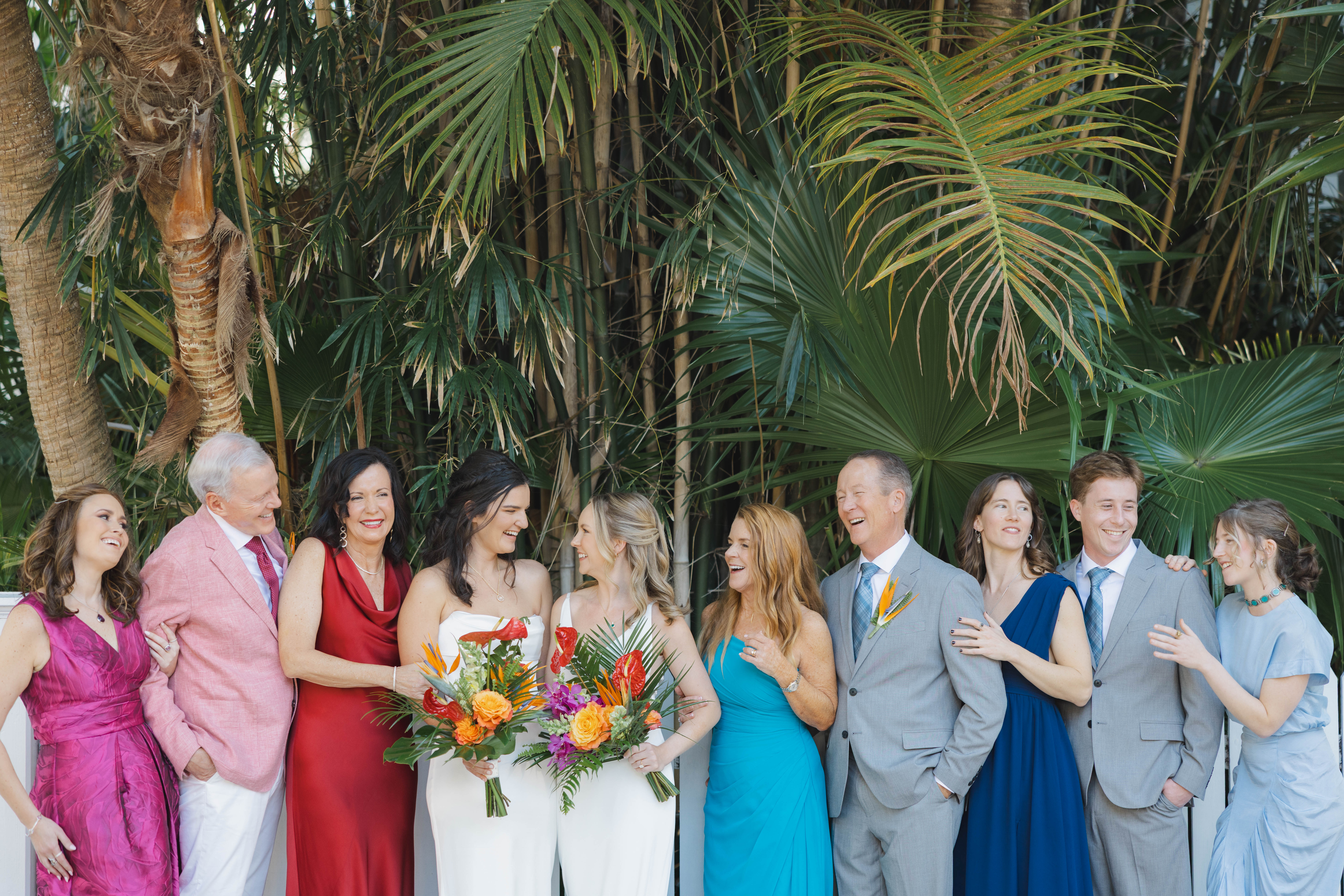 Brides with their families in brightly colored attire in front of a lush, green, tropical background.