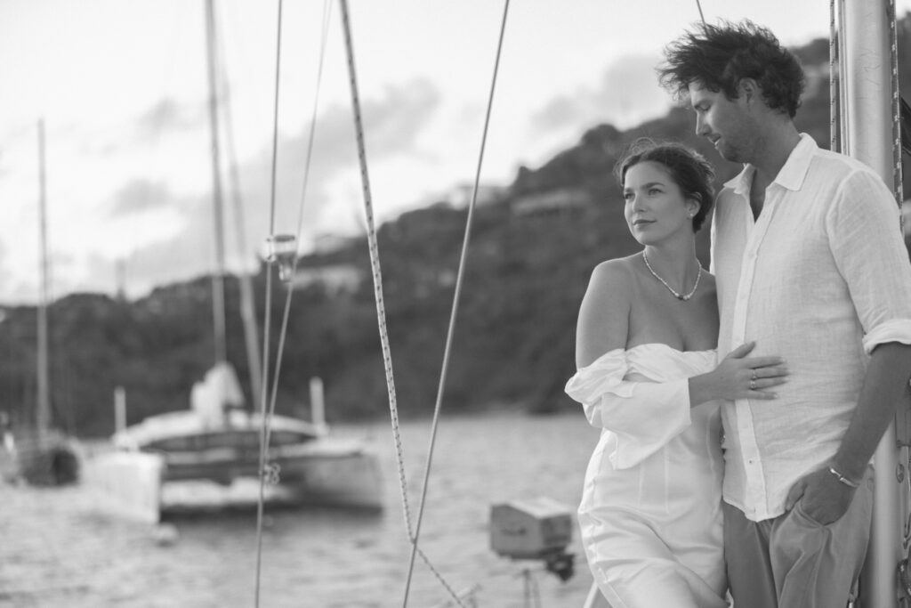 Black and white image of groom staring at his bride on their sailboat while the sun sets
