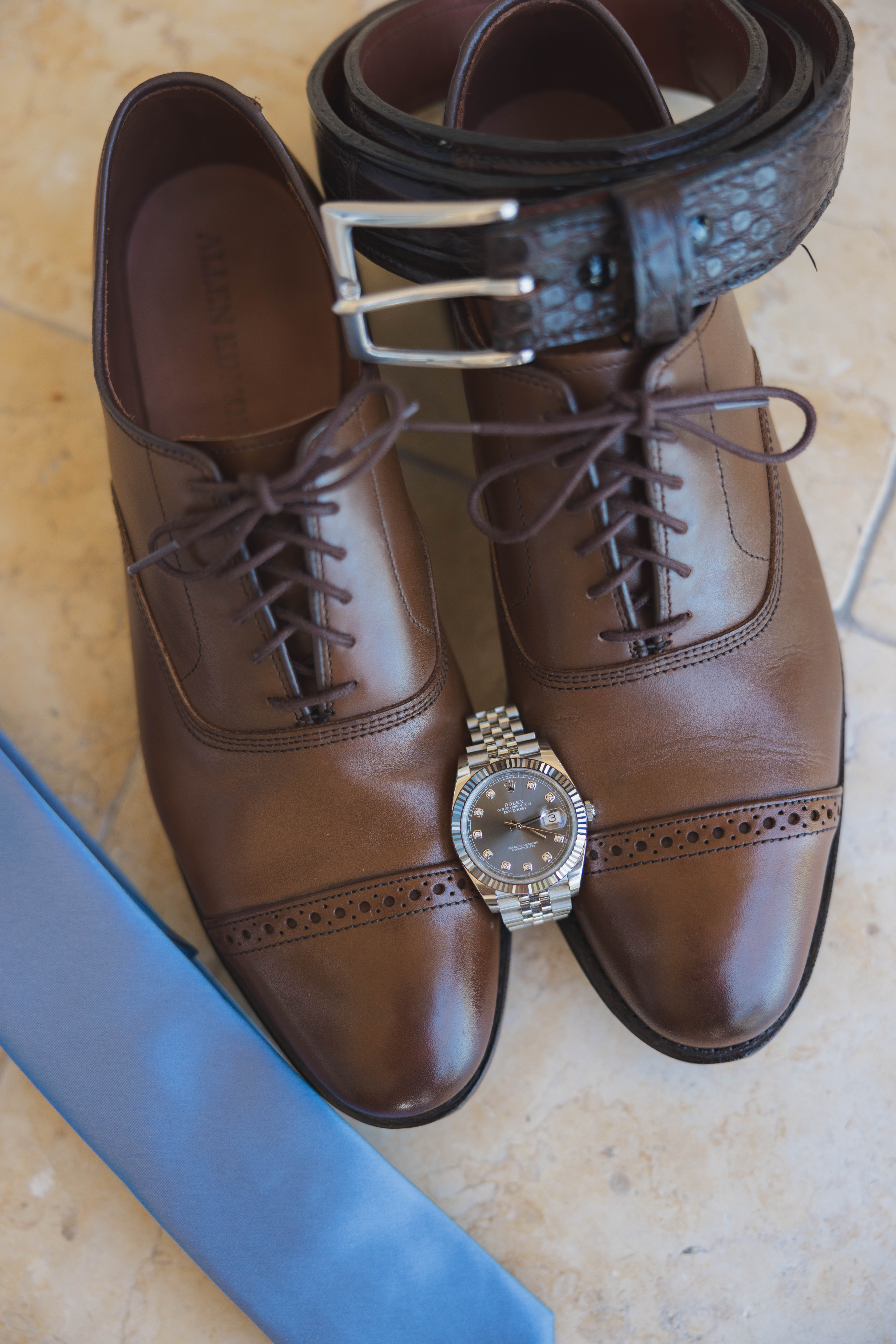 The groom's accessories, a blue tie, brown shoes, watch, and belt