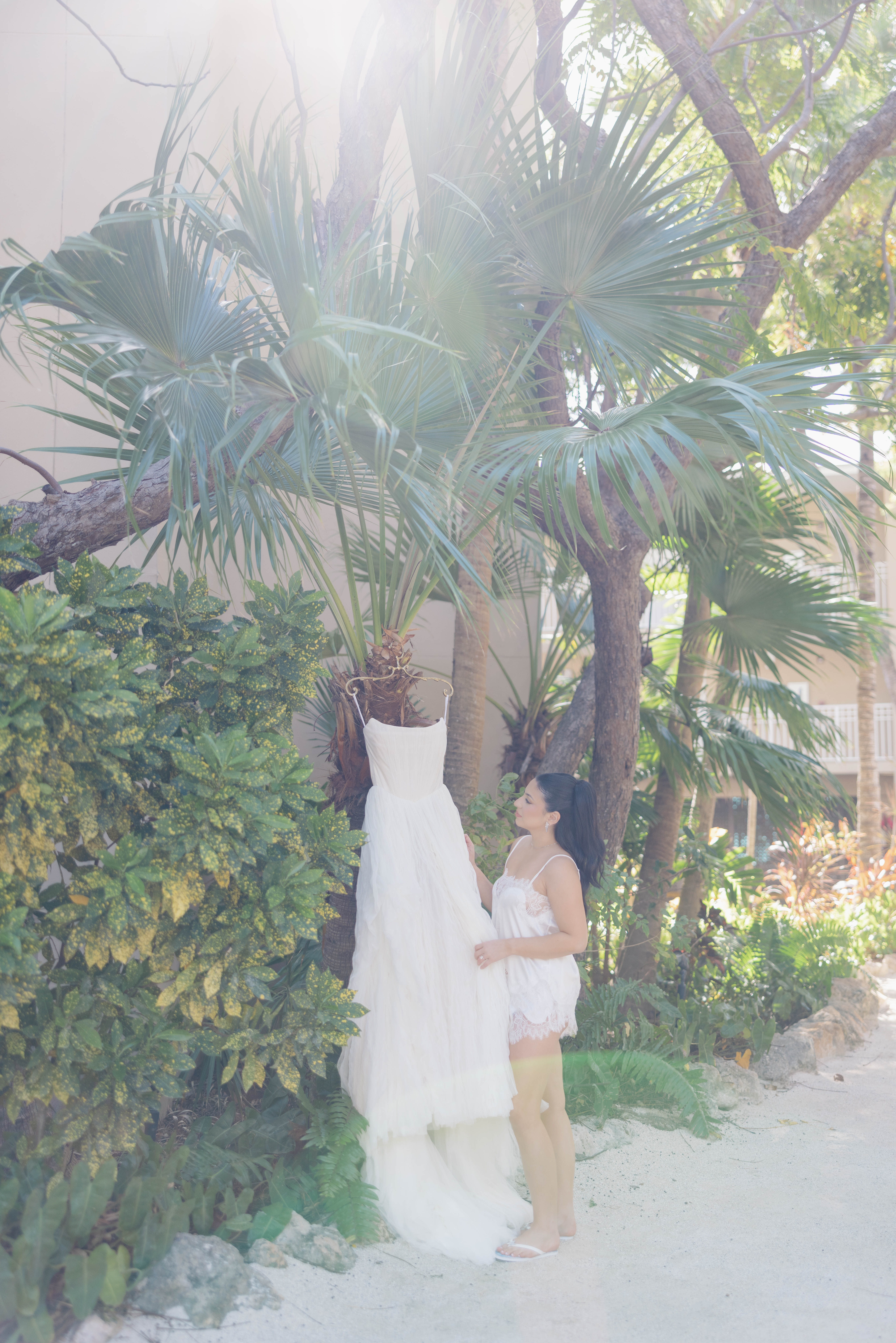 Bride admiring her white wedding dress amidst lush greenery and palm trees