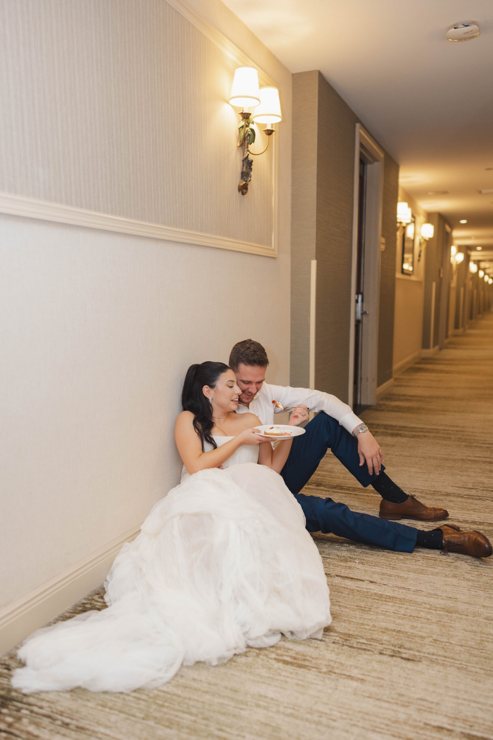 Bride and groom sharing wedding cake in the hallway during their reception