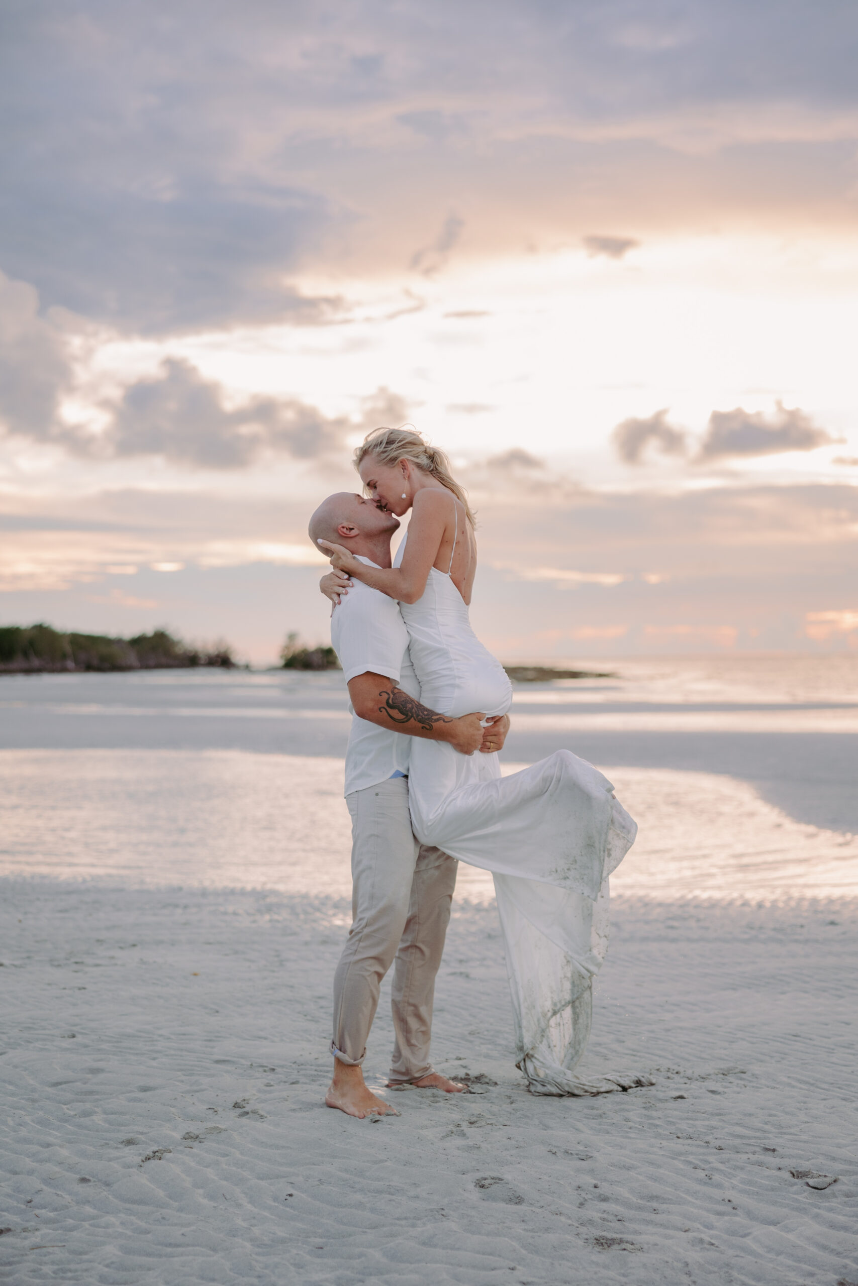 Man lifting woman in wedding dress on the beach